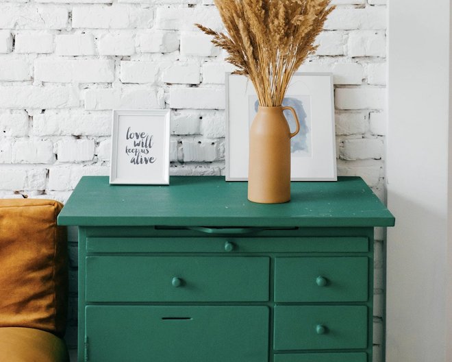 photo of a chest of drawers with framed art and a vase with foliage on top